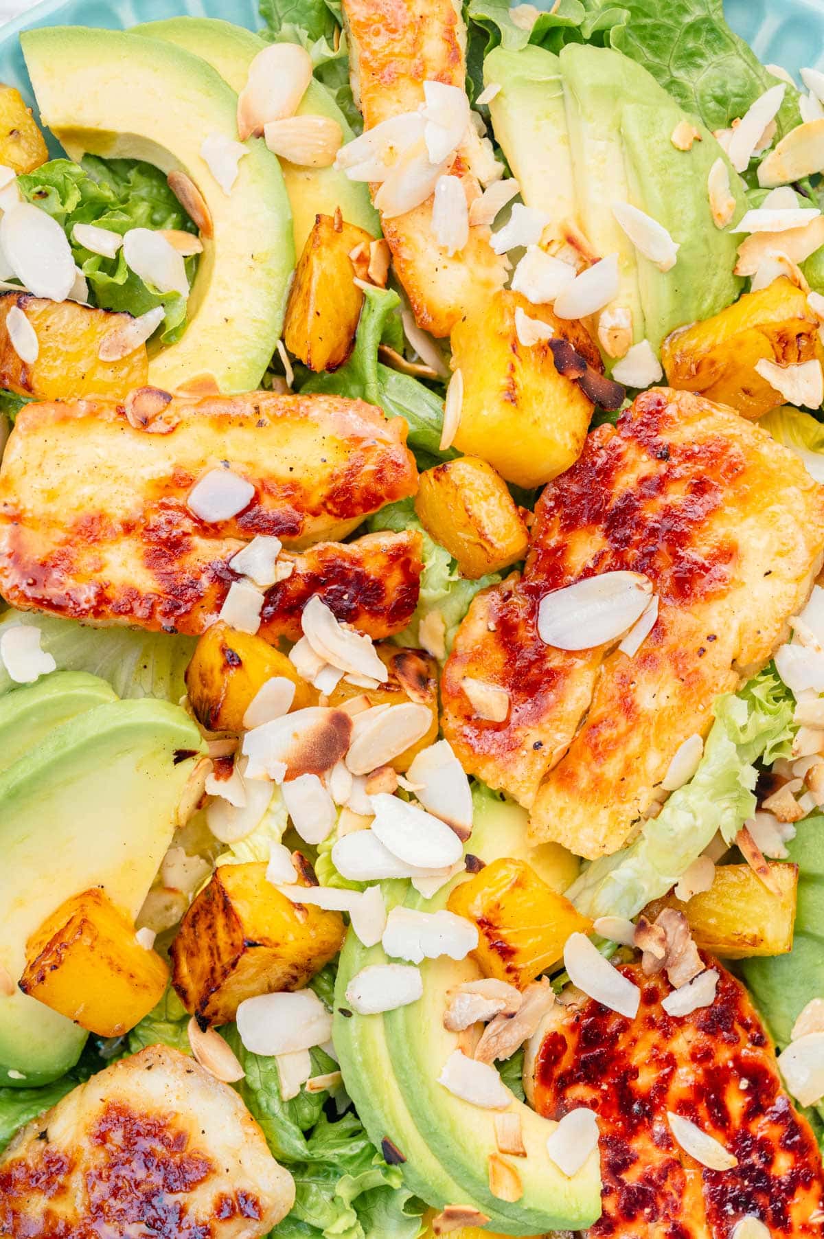 A close up photo of Halloumi Salad with pineapple and avocado on a blue plate.
