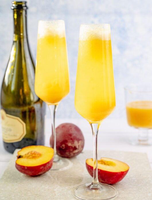 Two glasses with peach bellini on a stone board.