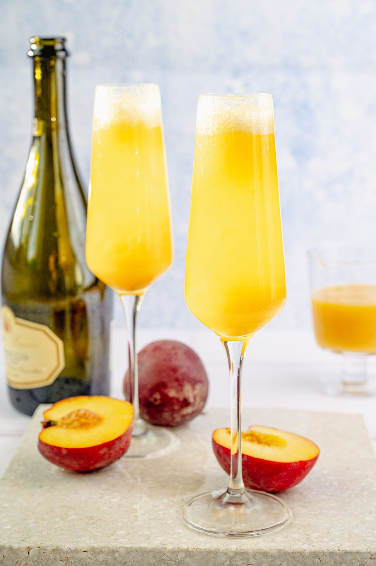 Two champagne glasses with peach bellini on a stone board. Prosecco bottle in the background.