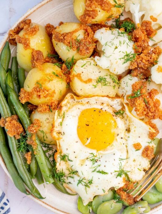 Green beans, potatoes, sunny-side-up egg, buttered breadcrumbs, cauliflower on a plate.