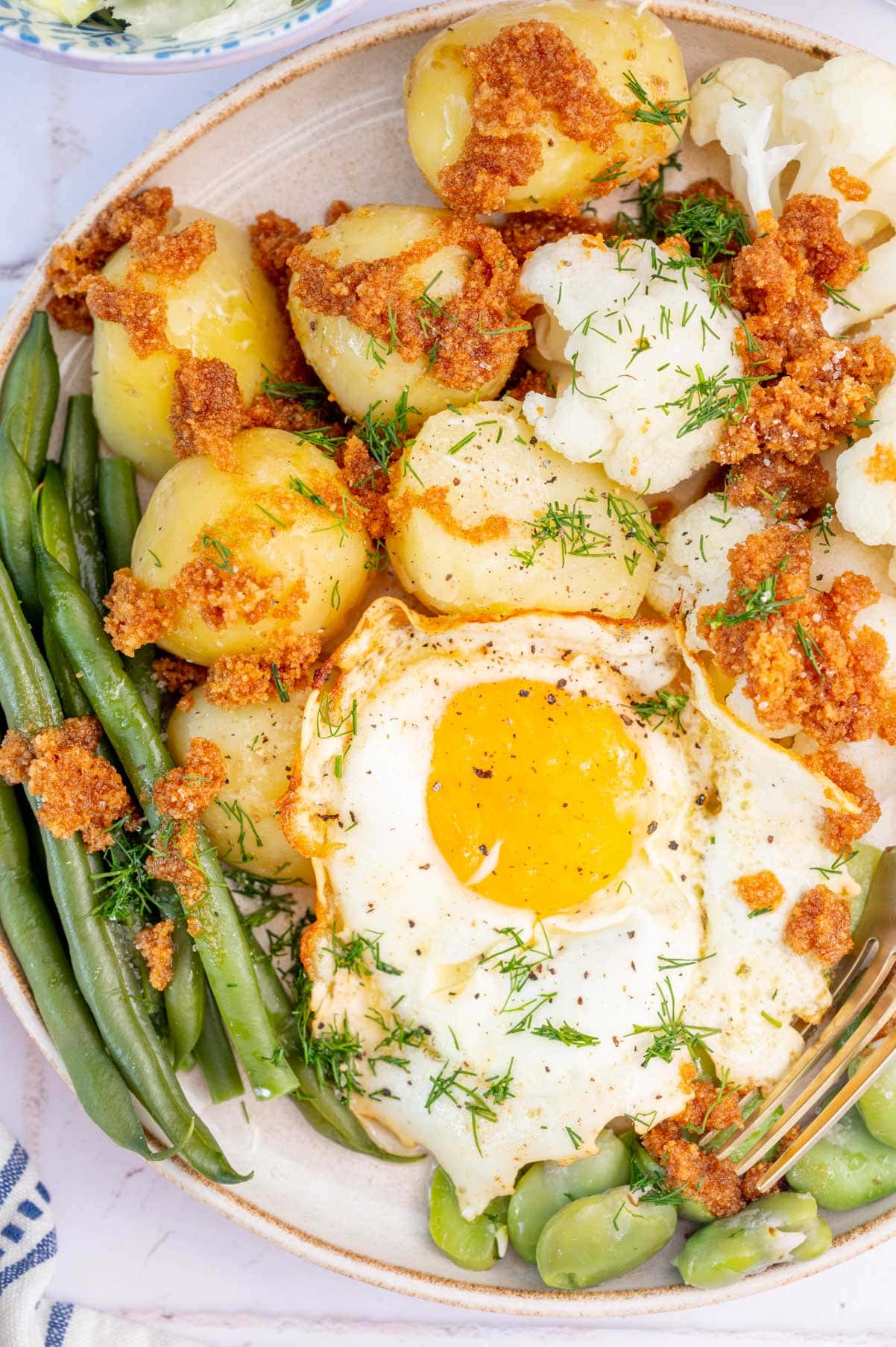 Green beans, potatoes, cauliflower, fava beans, sunny-side-up egg on a plate.