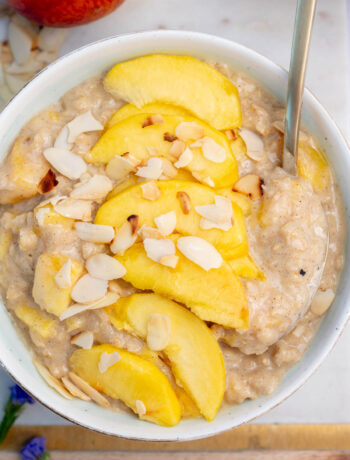 Peach oatmeal in a white bowl topped with peach slices and almond flakes.