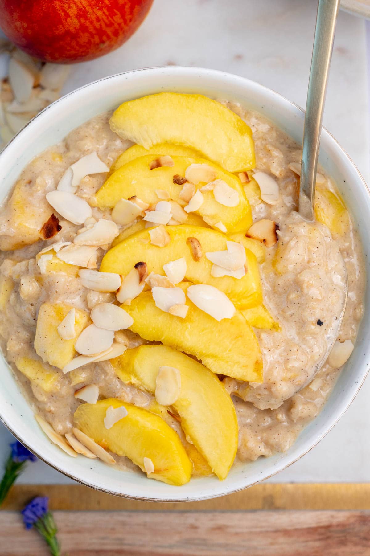 Peach oatmeal in a white bowl topped with peach slices and almond flakes.