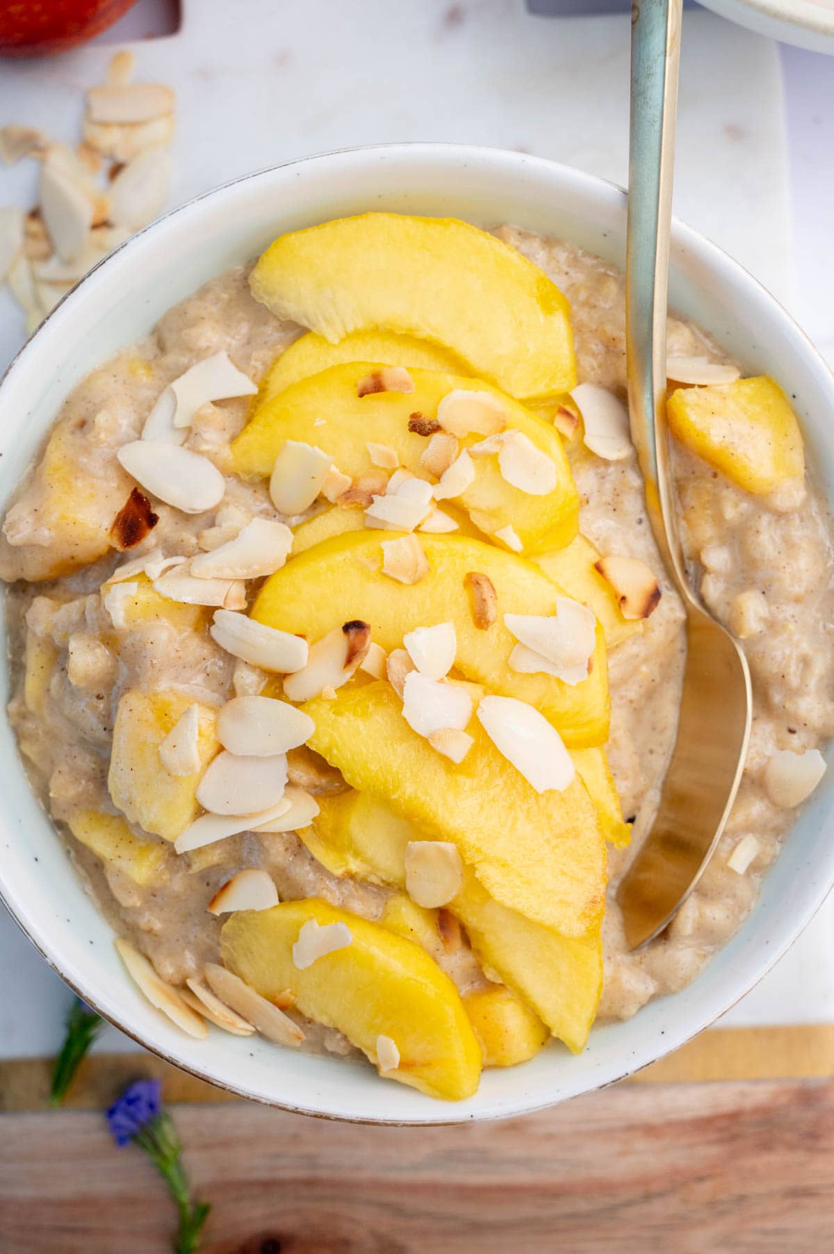 Peach oatmeal in a white bowl topped with peach slices and almond flakes.