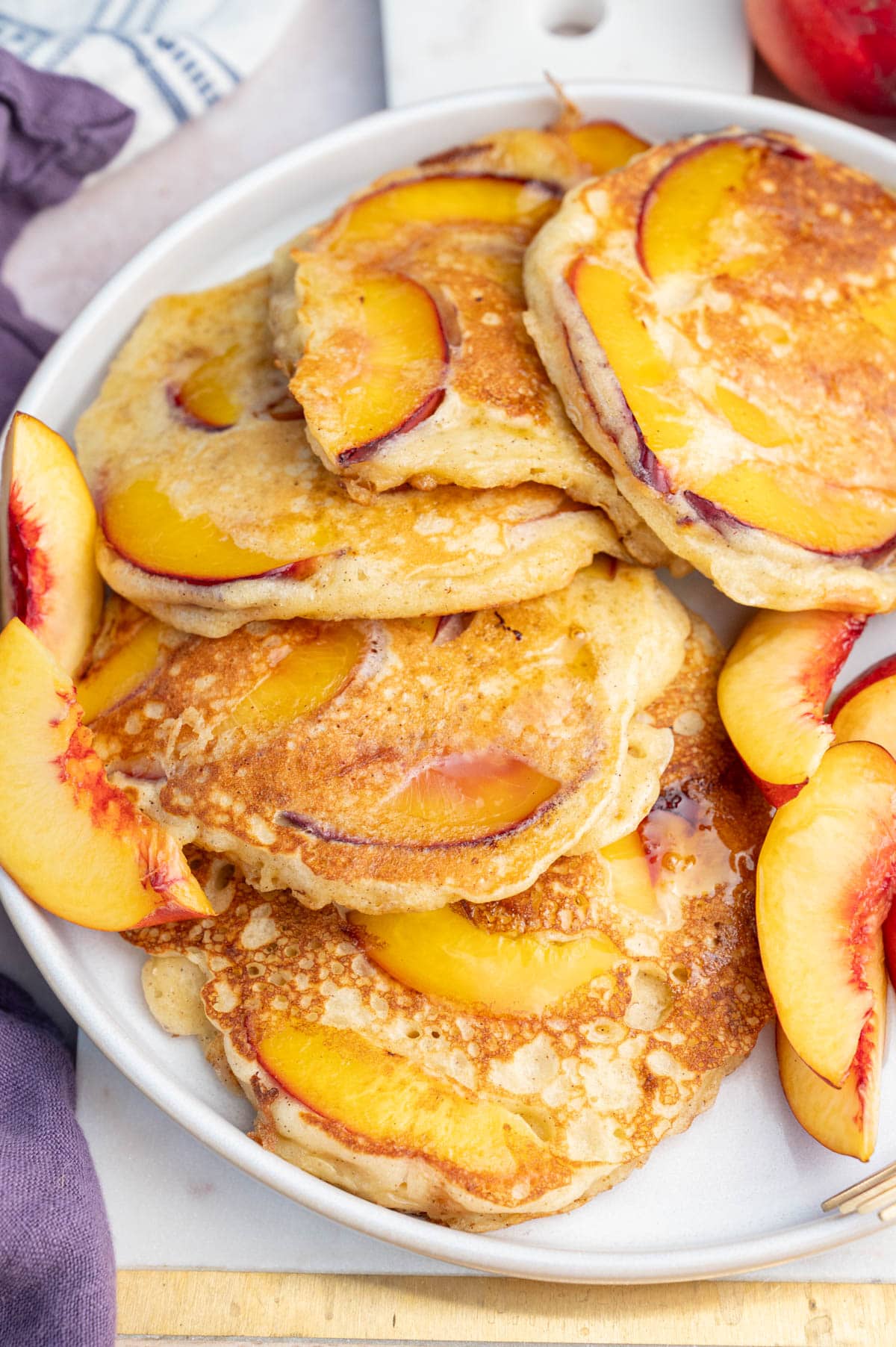 Peach pancakes on a white plate with fresh peach wedges on the side.