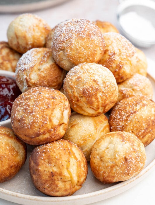Aebleskiver Danish pancake balls on a beige plate dusted with powdered sugar.