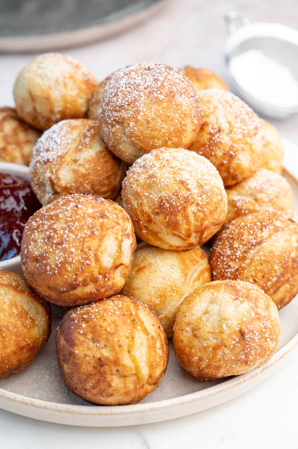 Aebleskiver - Danish Pancake Balls on a beige plate dusted with powdered sugar.