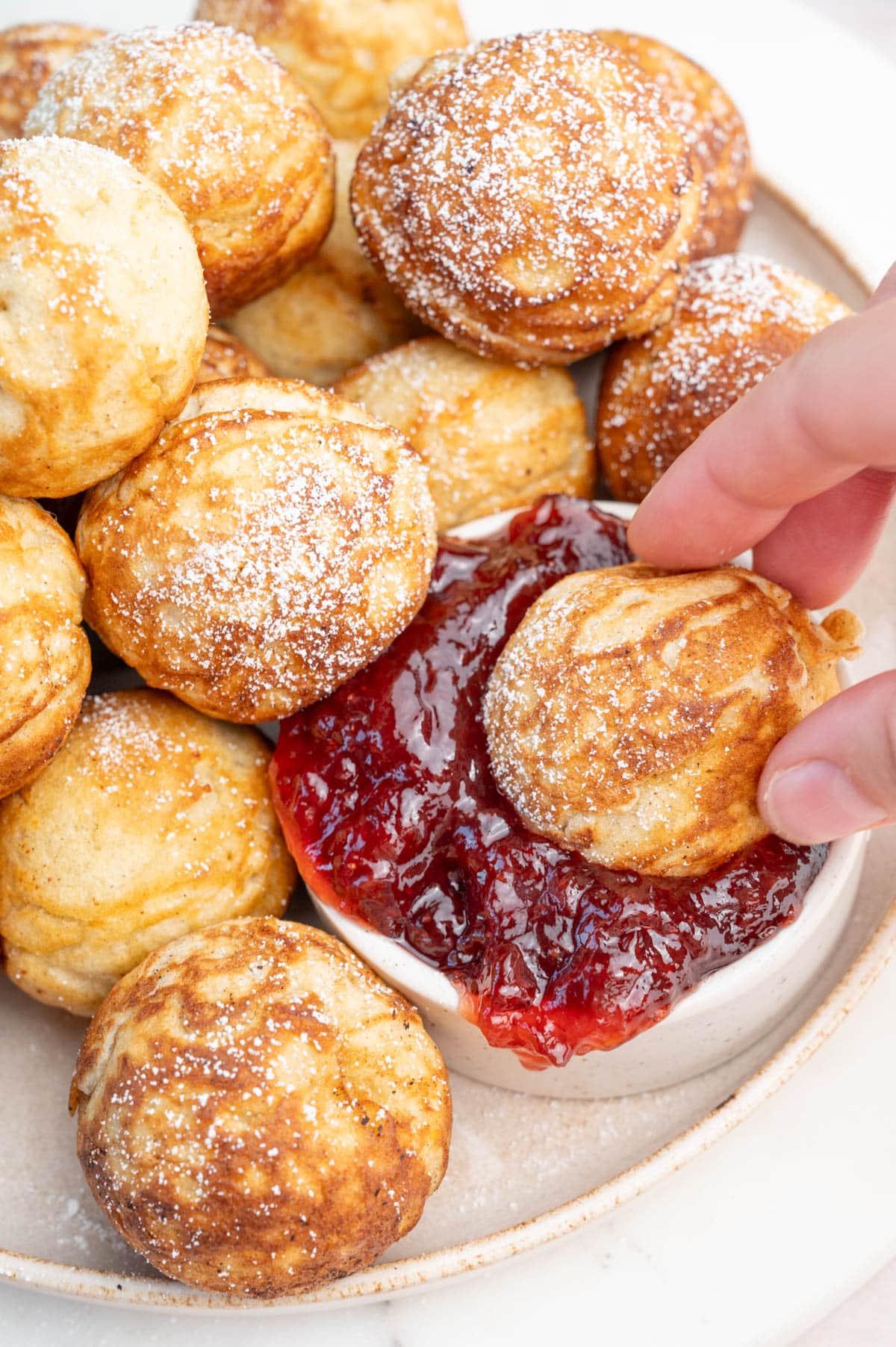 Aebleskiver pancake ball is being dipped in strawberry jam.