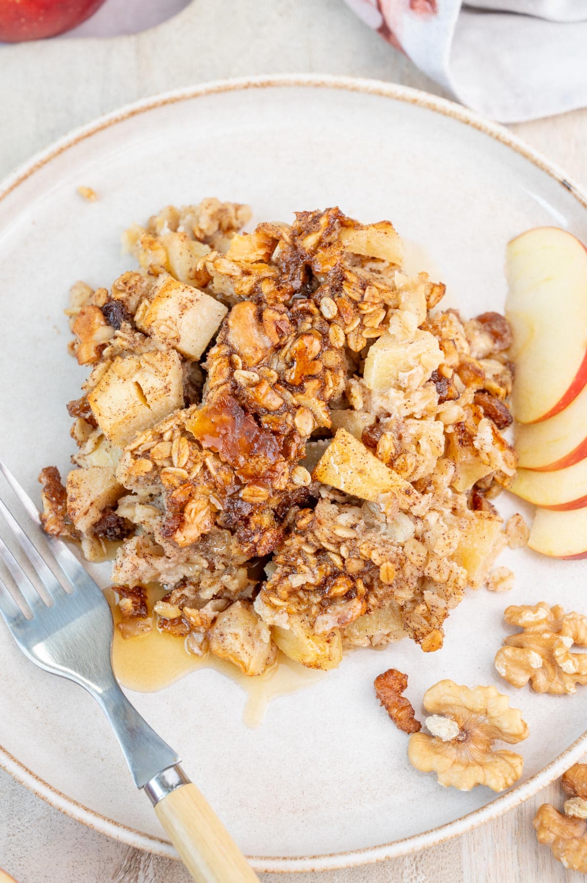 One serving of apple baked oatmeal on a white plate with apple slices on the side.