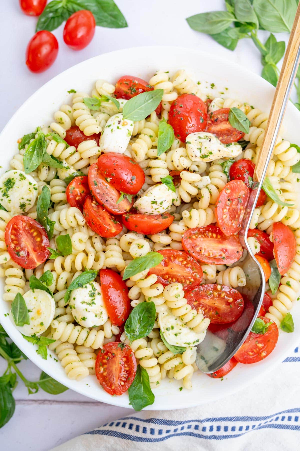 Caprese Pasta Salad in a large white bowl with a spoon on the side.