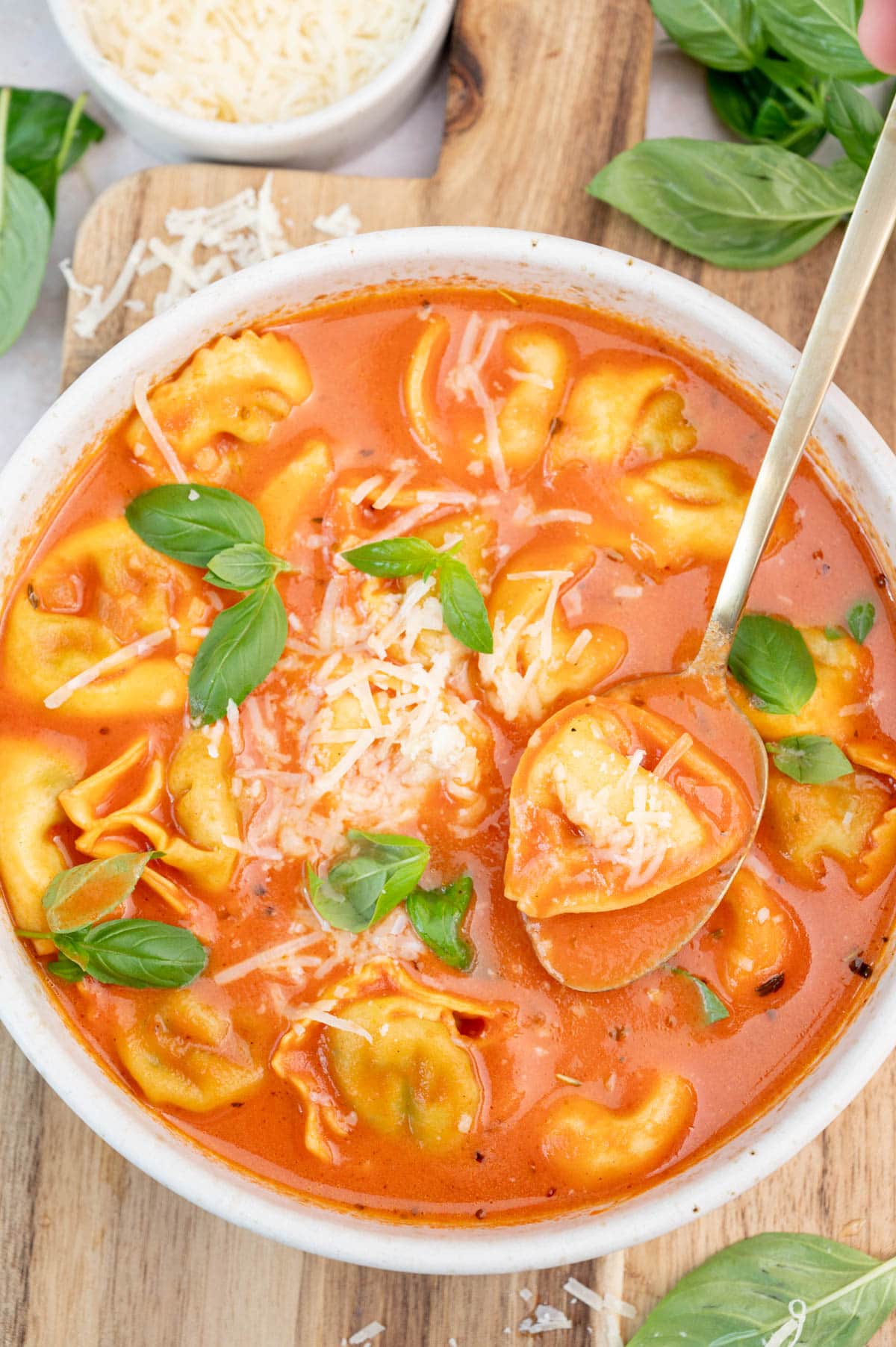 Tomato tortellini soup in a white bowl sprinkled with parmesan and basil leaves.