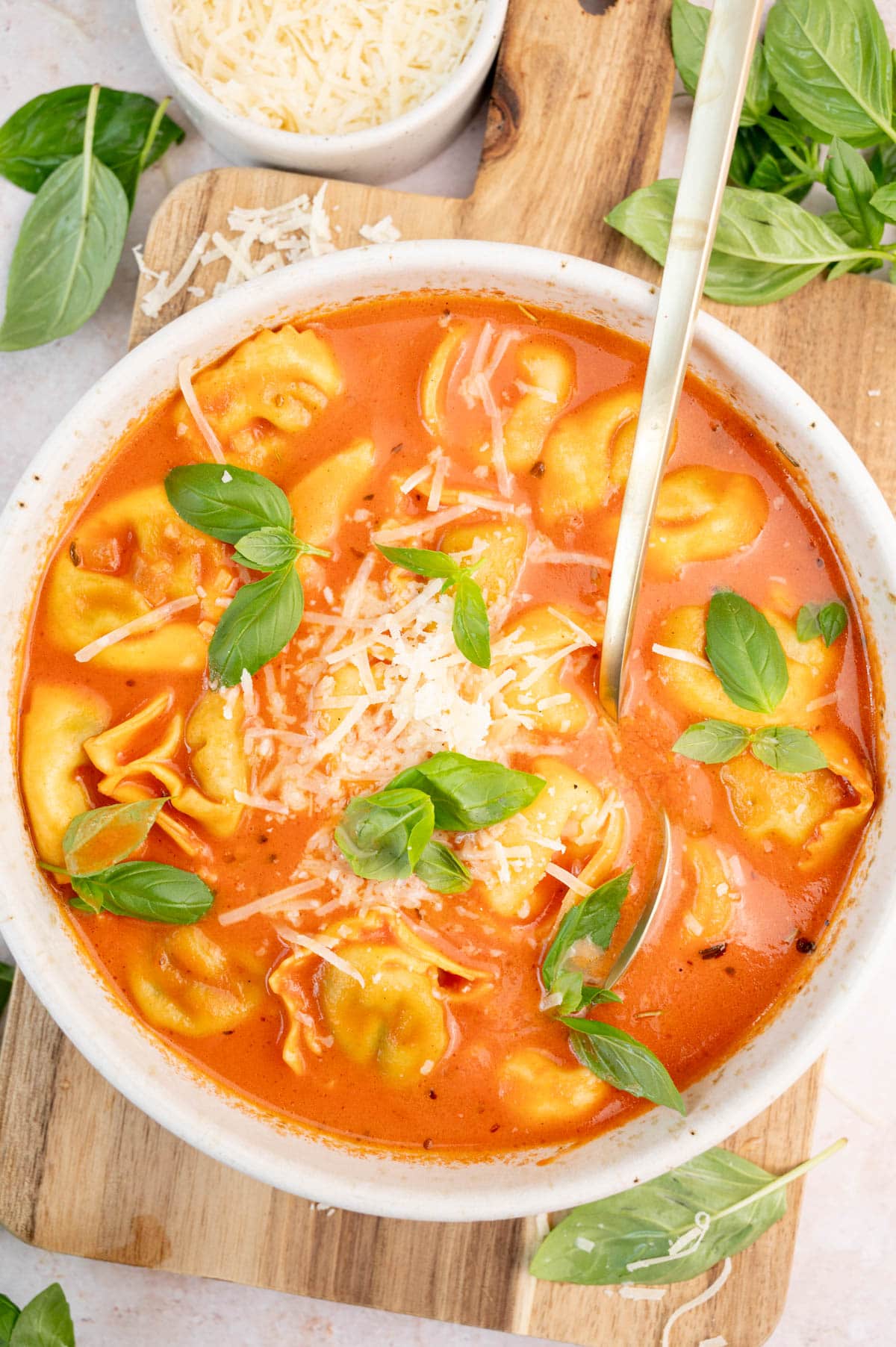 Tomato tortellini soup topped with grated parmesan and basil leaves in a white bowl.
