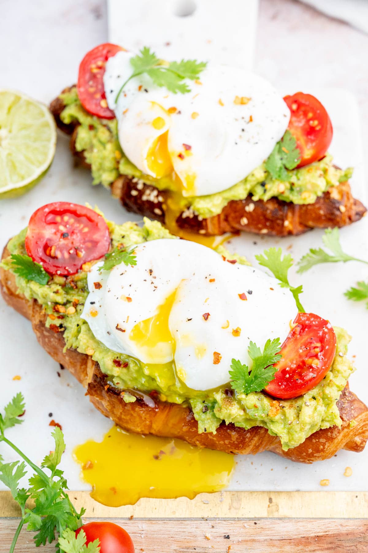 Two avocado egg toasts on a white board.