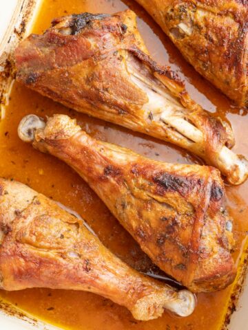 Baked turkey drumsticks in a white baking dish.