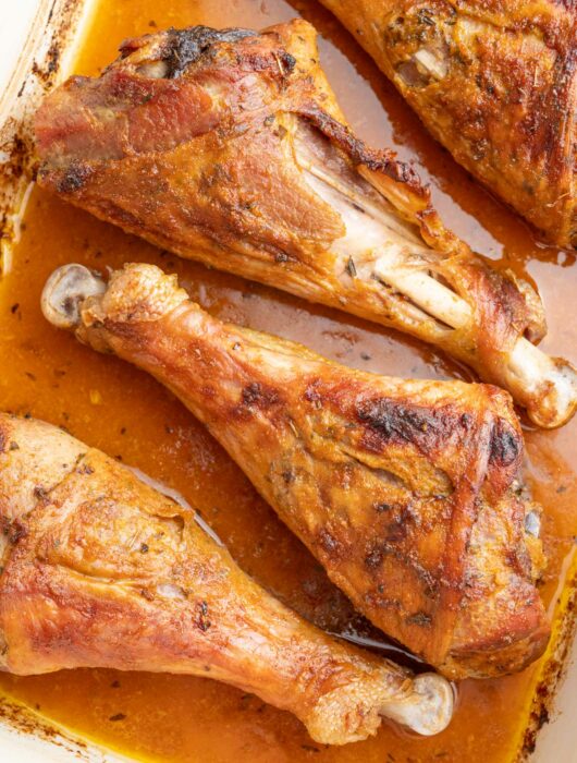 Baked turkey drumsticks in a white baking dish.