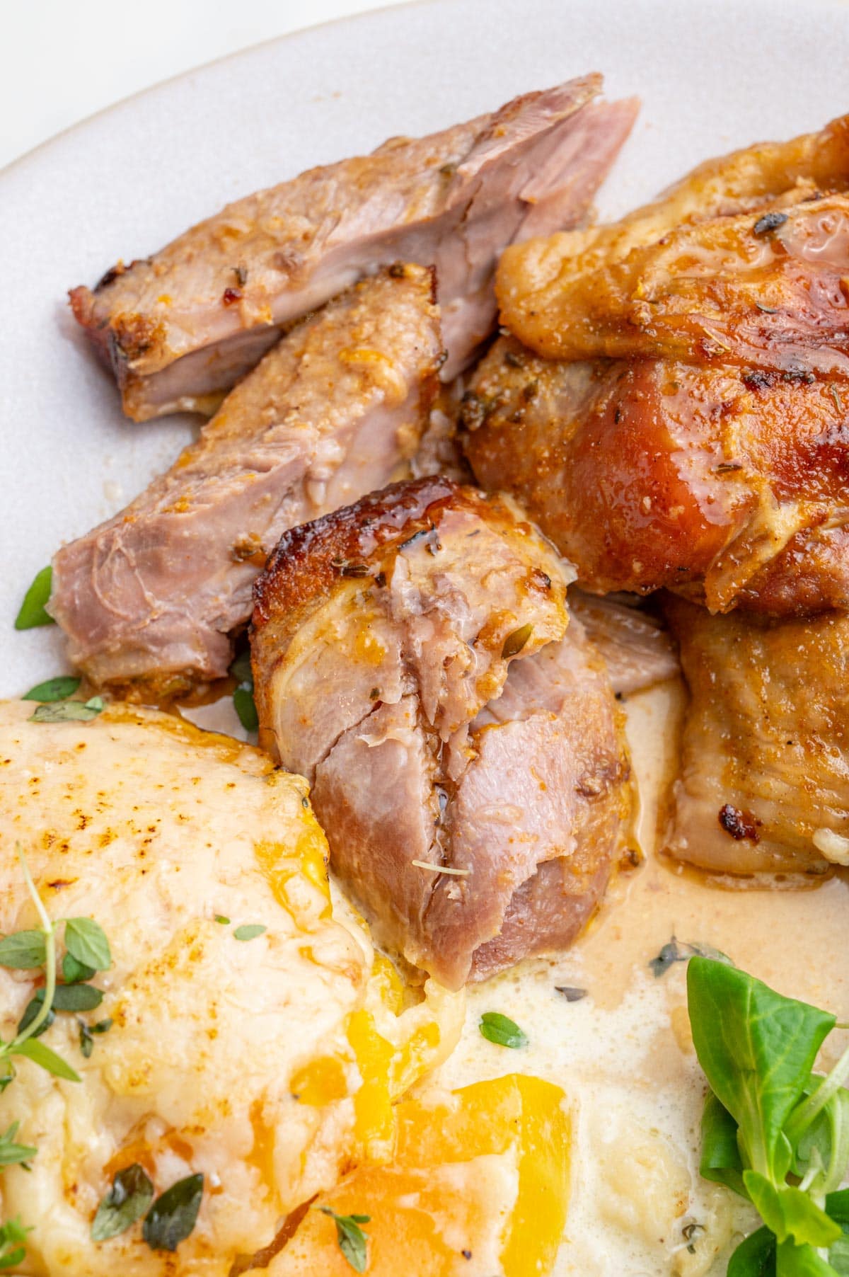 A close-up photo of baked turkey drumsticks on a beige plate with roasted butternut squash and salad.