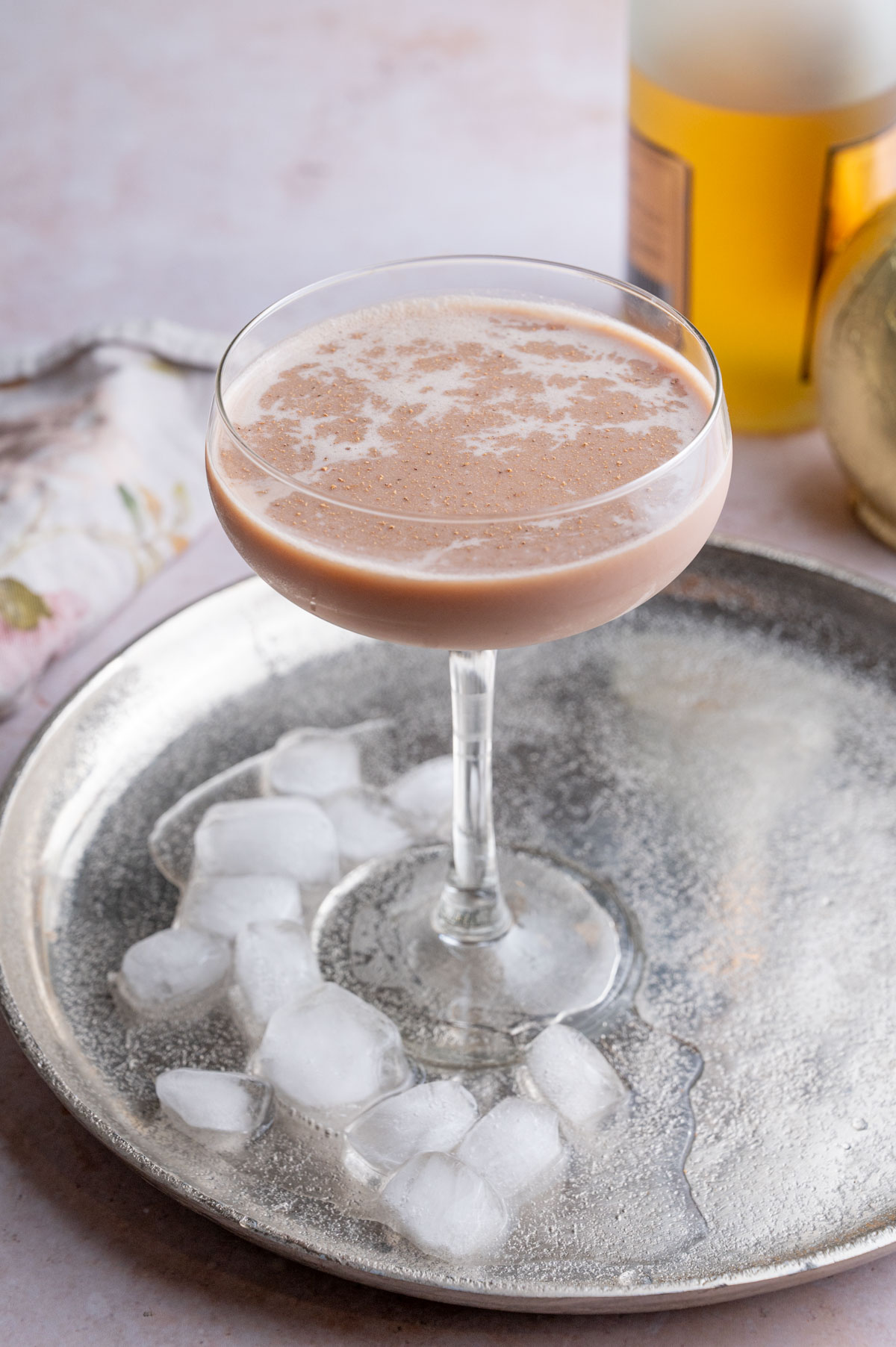 Brandy Alexander cocktail in a coupe glass on a silver tray with ice cubes.