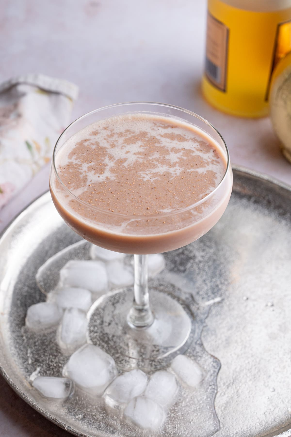 Brandy Alexander cocktail in a coupe glass on a silver tray with ice cubes.