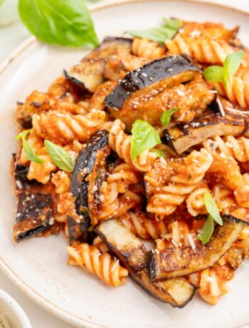 Pasta alla Norma on a white plate sprinkled with basil and parmesan.