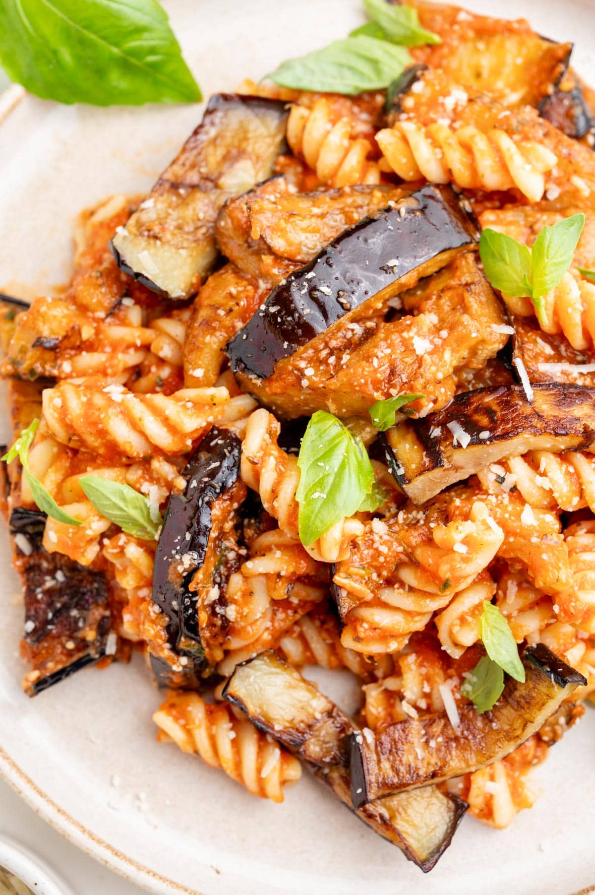 Pasta alla Norma on a white plate sprinkled with parmesan and basil leaves.