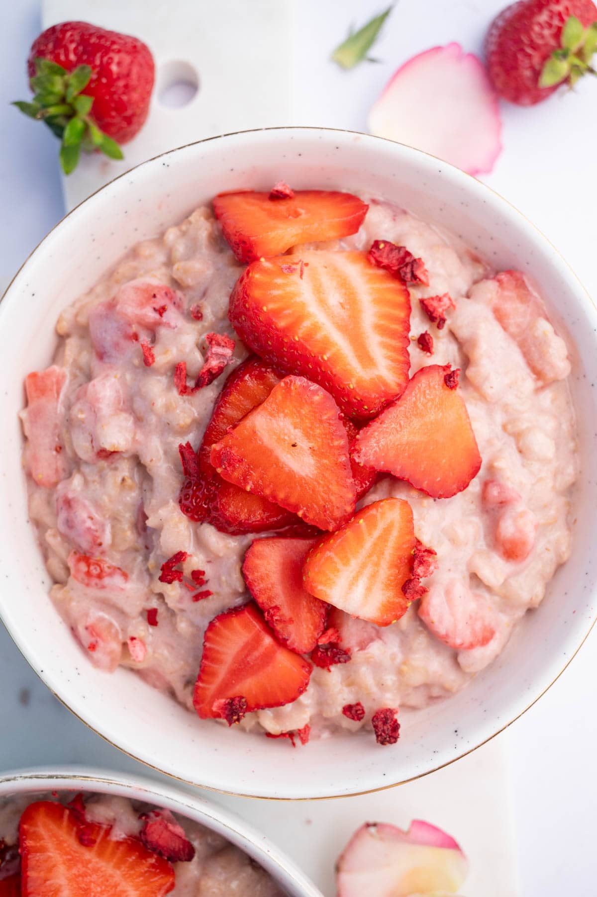 Strawberry oatmeal topped with strawberry slices and freeze-dried strawberries in a white bowl.