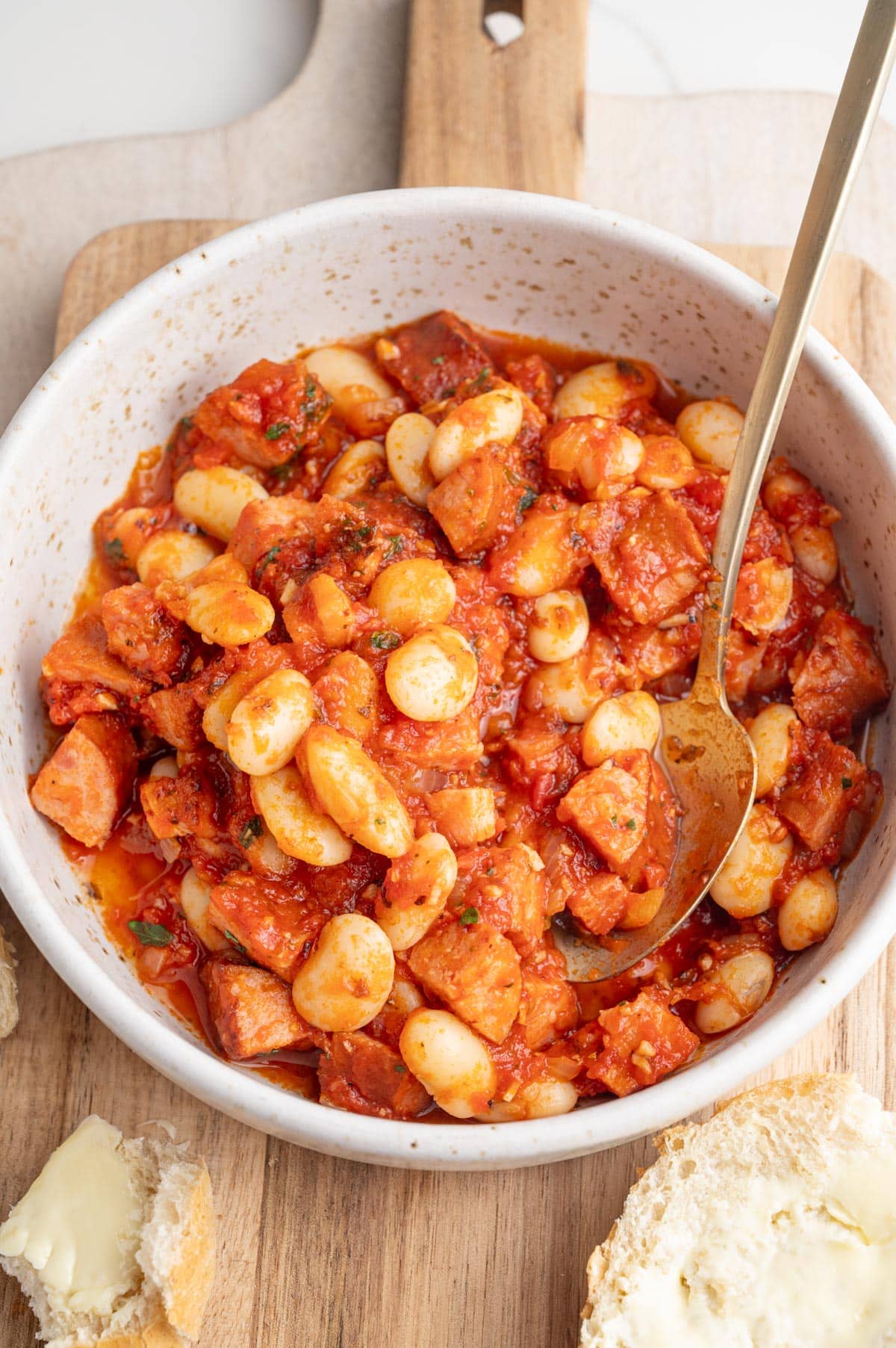 Polish beans and sausage in a white bowl on a wooden board.