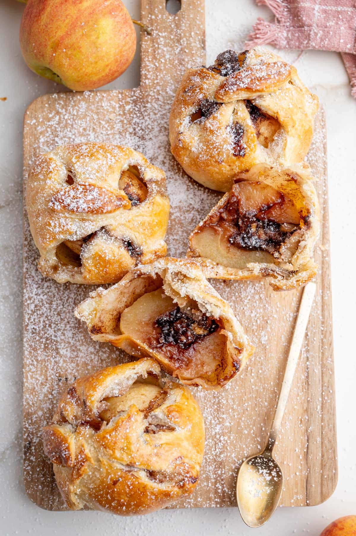An overhead photo of apples in puff pastry with chocolate filling on a wooden board sprinkled with powdered sugar.