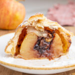 An apple wrapped in puff pastry with chocolate filling cut in half on a white plate.