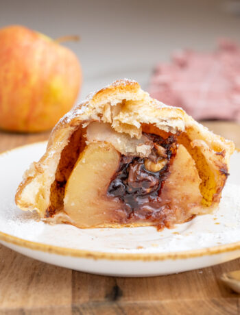 An apple wrapped in puff pastry with chocolate filling cut in half on a white plate.