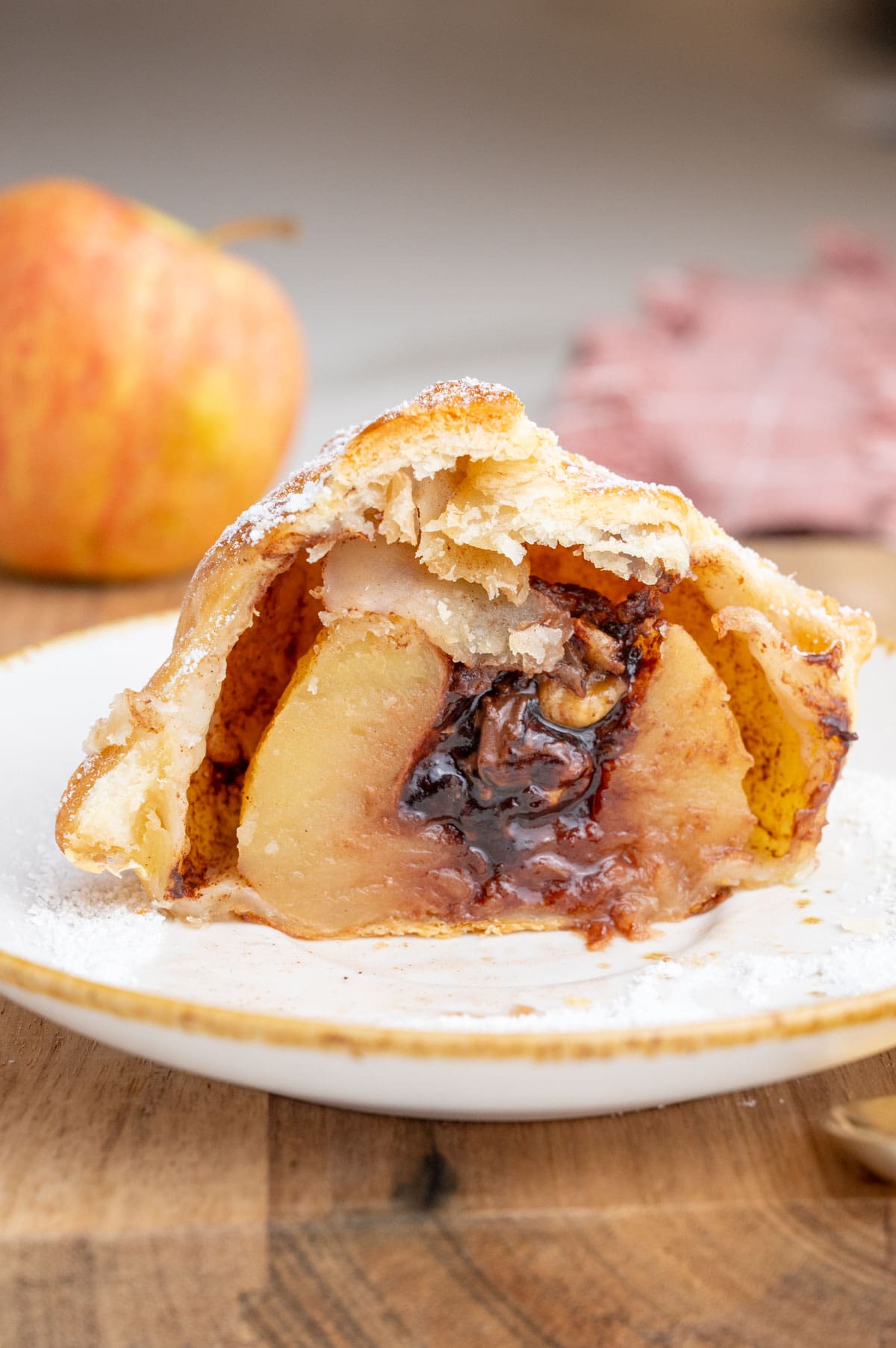 An apple wrapped in puff pastry with chocolate filling cut in half on a white plate.