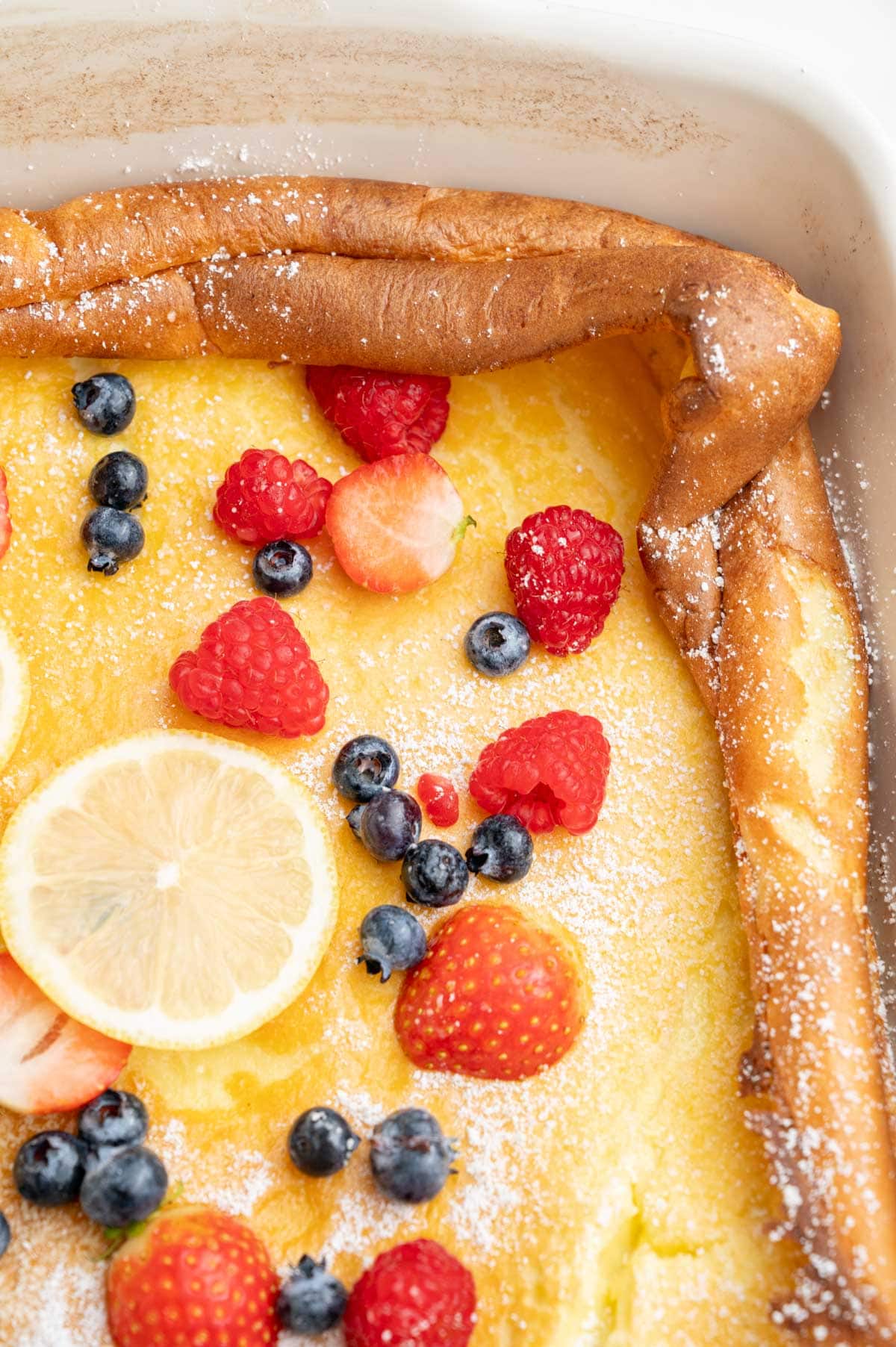 A close up photo of Dutch Baby pancake in a white casserole dish topped with berries.