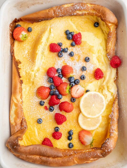 Dutch baby pancake in a white casserole dish topped with berries.