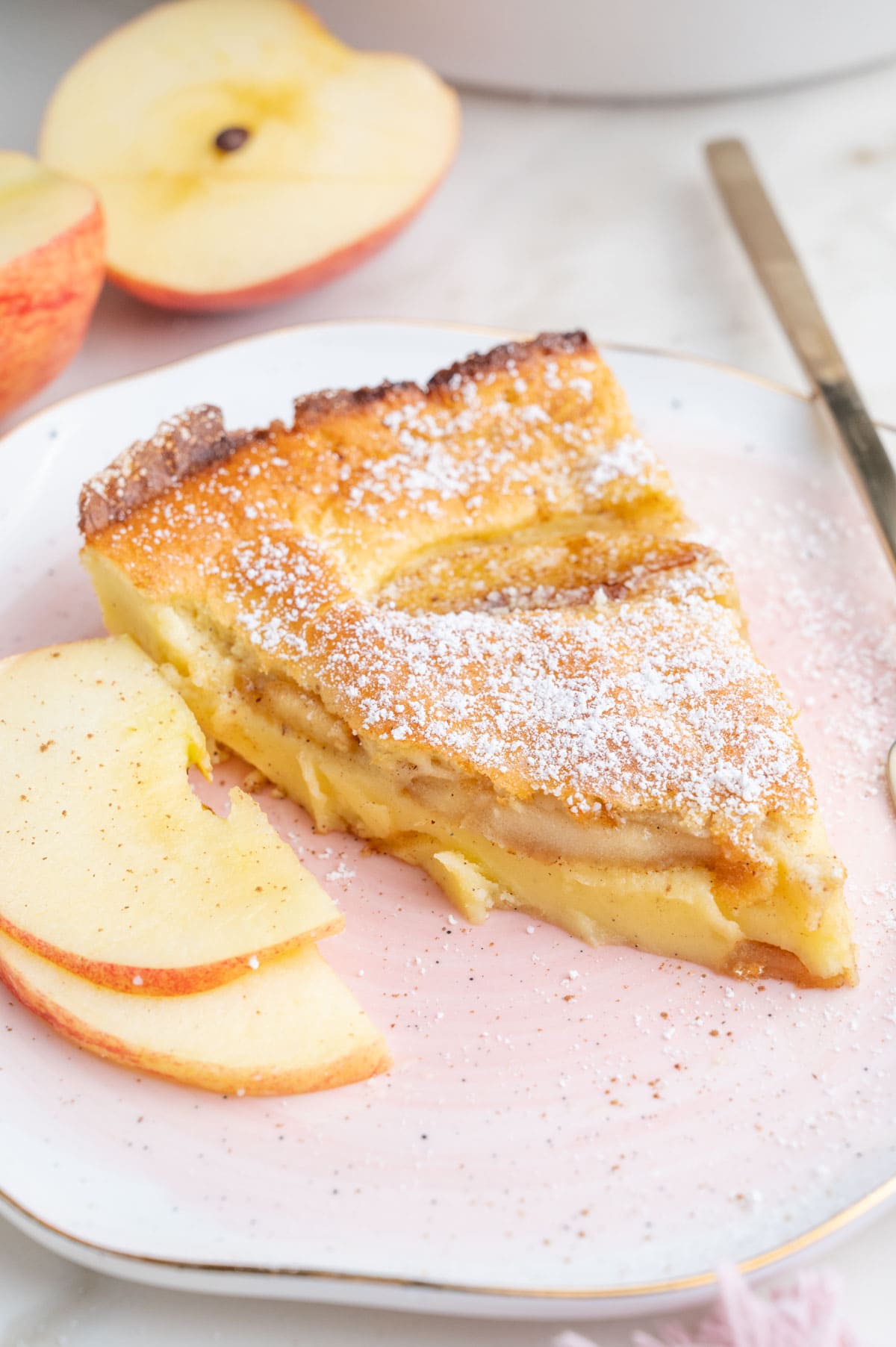 One slice of German apple pancake on a pink plate with apple slices on the side.