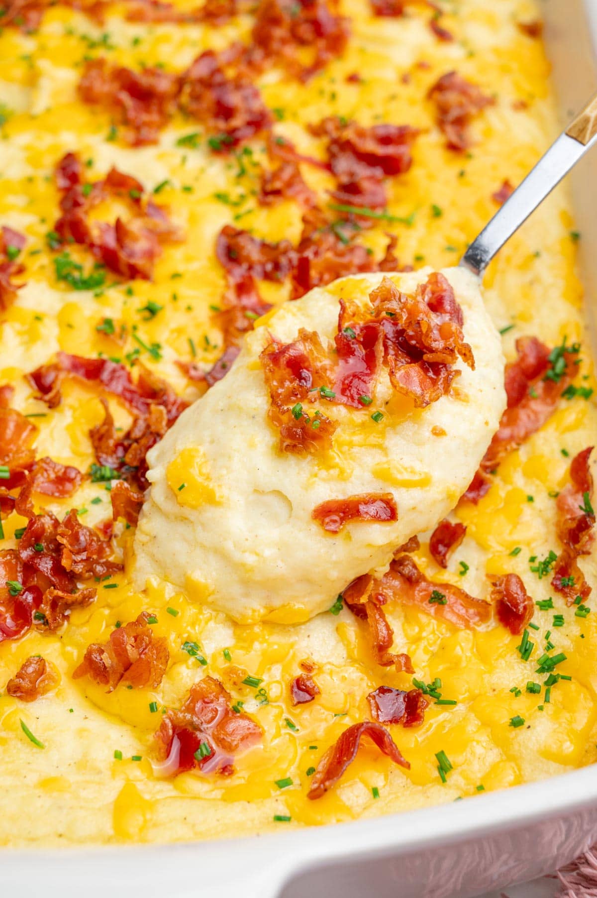 A close up photo of loaded mashed potato casserole in a white baking dish.