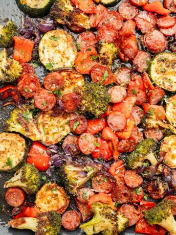 Roasted sausage slices and chopped vegetables on a baking sheet.