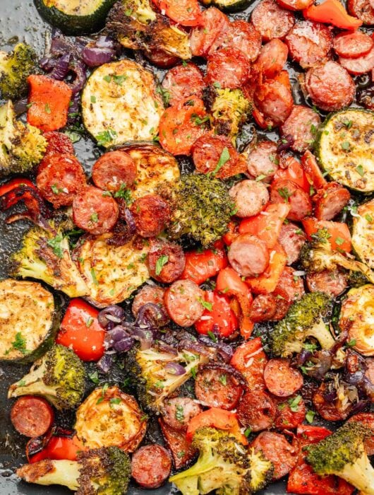 Roasted sausage slices and chopped vegetables on a baking sheet.