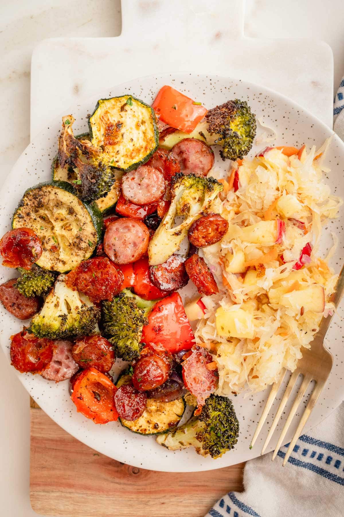 Roasted sausage and vegetables with sauerkraut apple salad on a white plate.