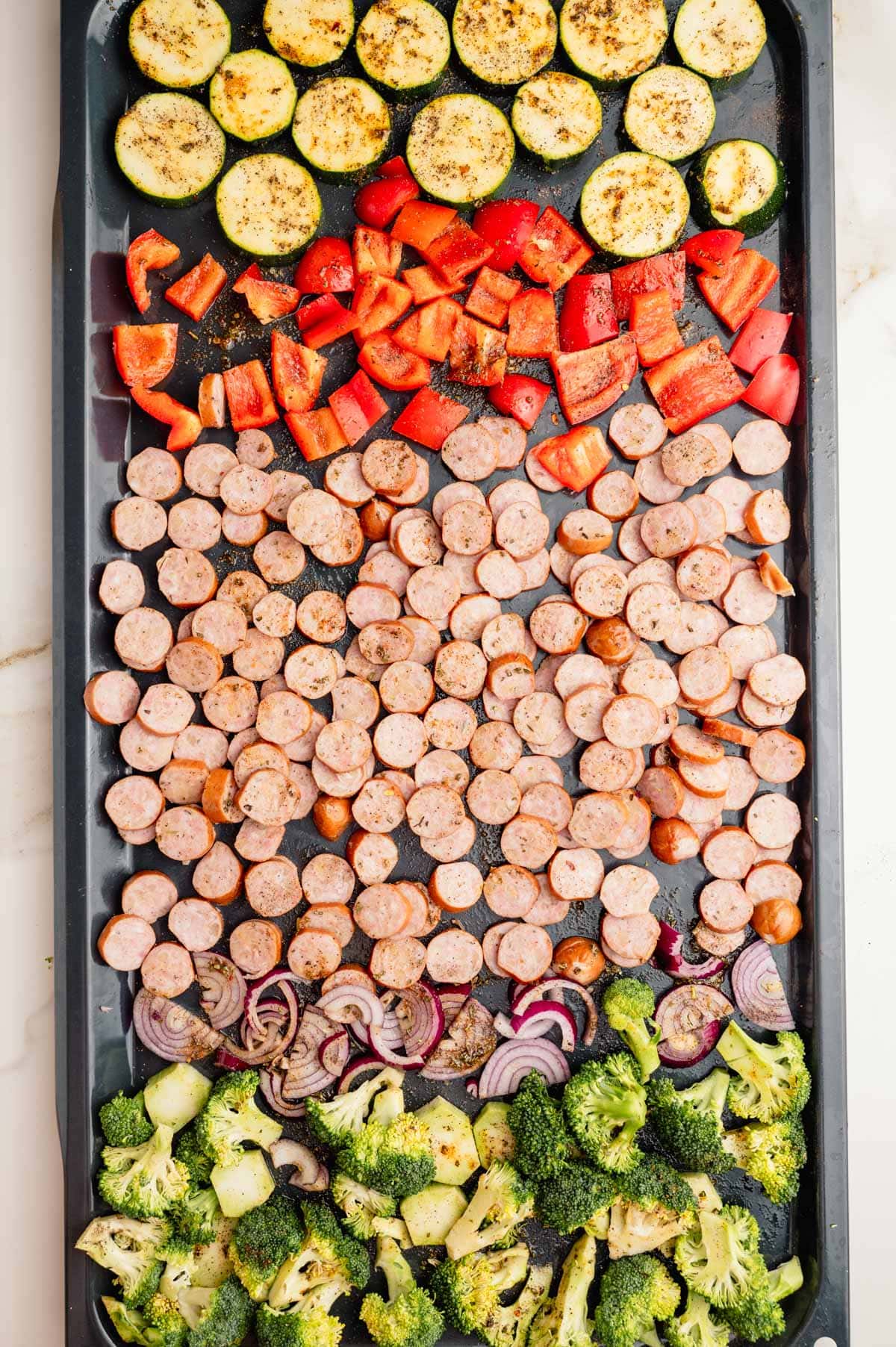 Sliced sausage and seasoned chopped vegetables on a baking sheet ready to be baked.