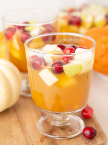 Two glasses with Thanksgiving sangria on a wooden board. Mini pumpkins and cranberries in the background.