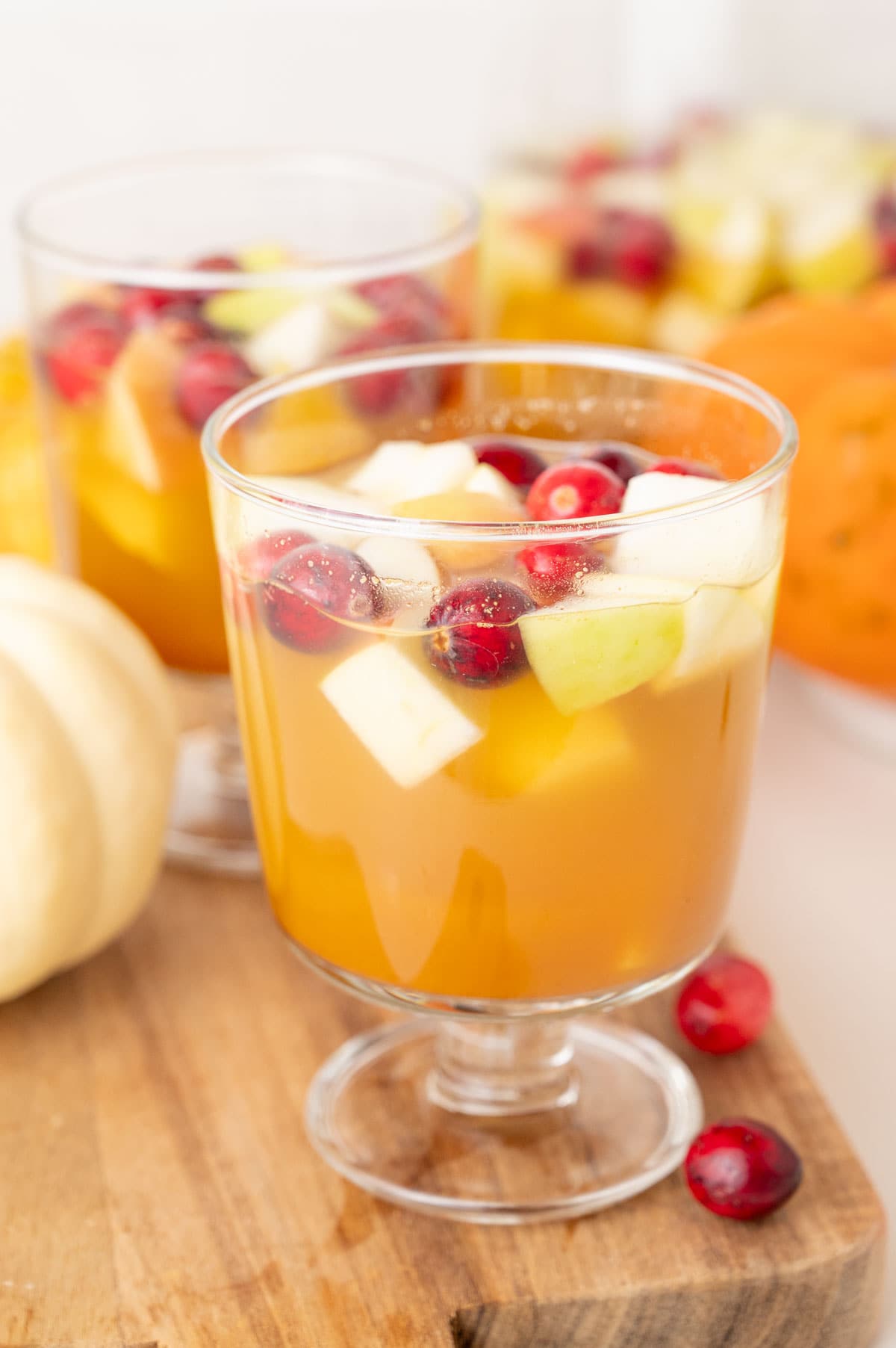 Two glasses with Thanksgiving sangria on a wooden board. Mini pumpkins and cranberries in the background.