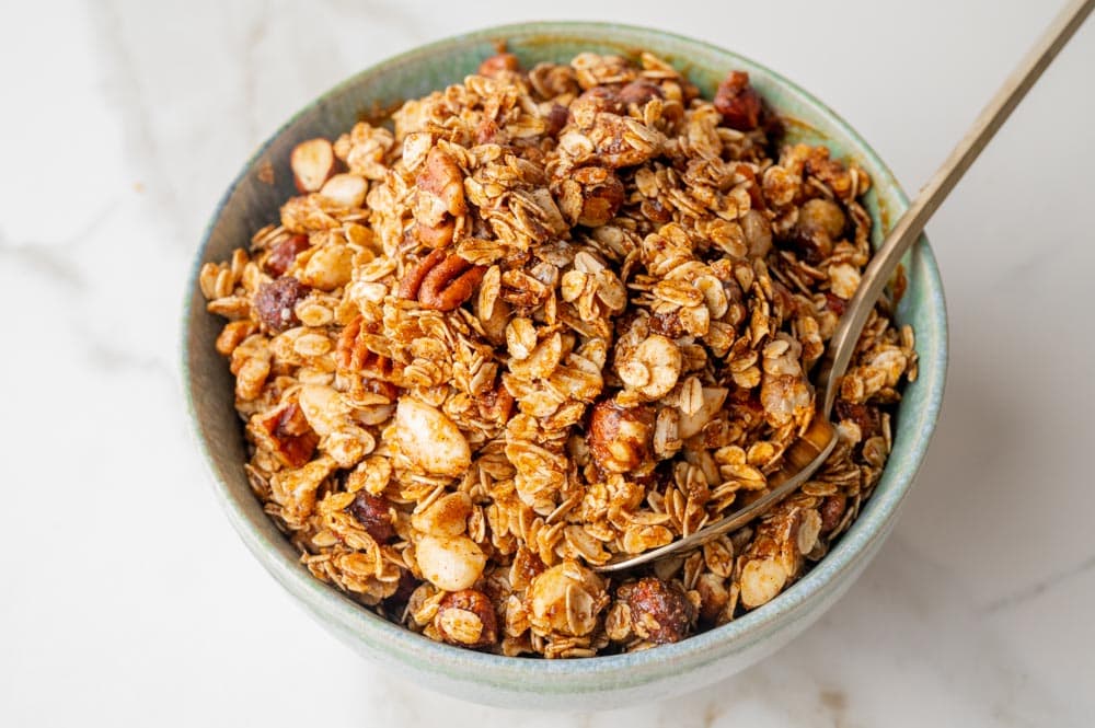 A mixture of oats, nuts, seasoning, and sweeteners in a bowl.
