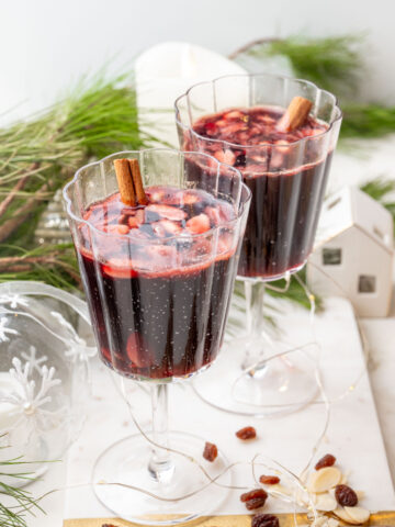 Two glasses with Glogg - Scandinavian mulled wine on a white board. Christmas decorations in the background.