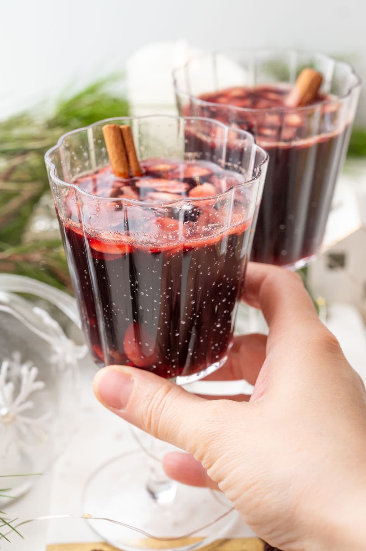 A glass with Glogg is being held in a hand. Christmas decorations in the background.