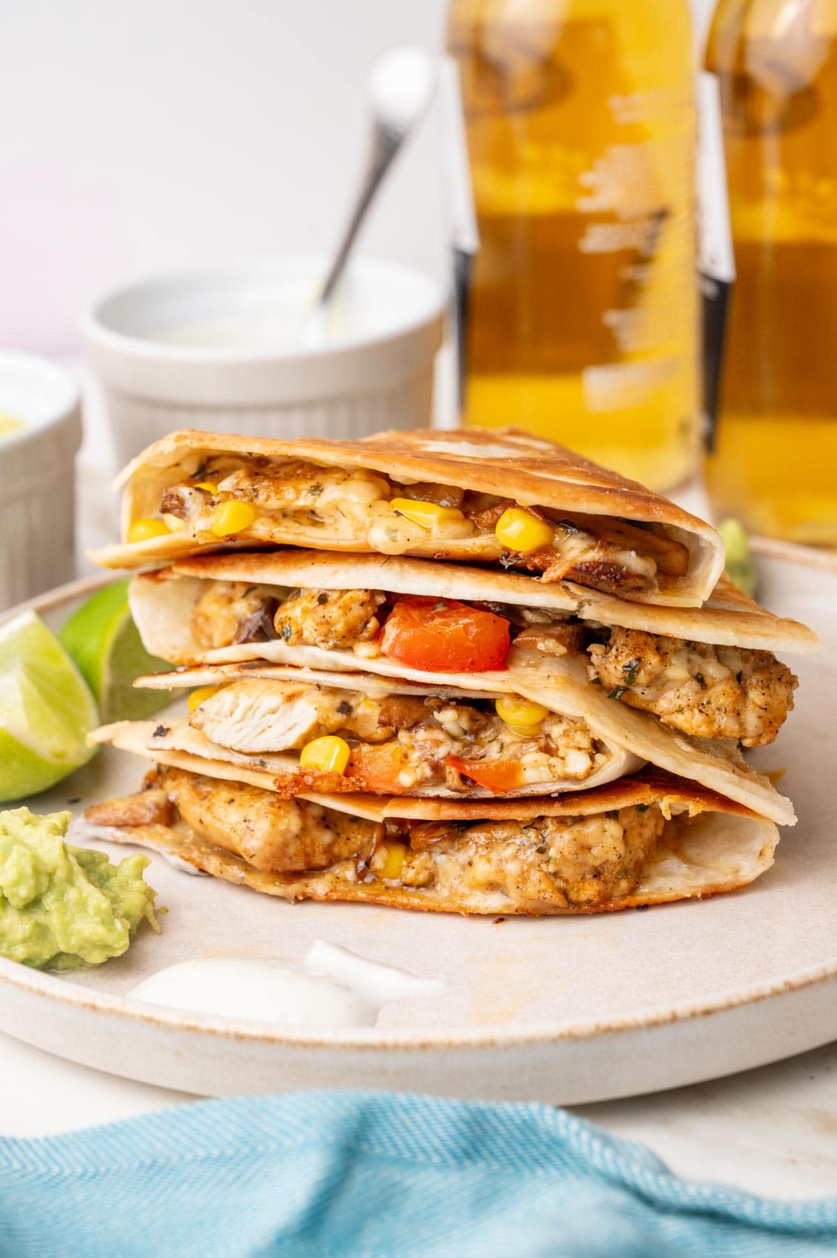 A stack of chicken quesadillas on a beige plate. Guacamole and sour cream dip on the side.