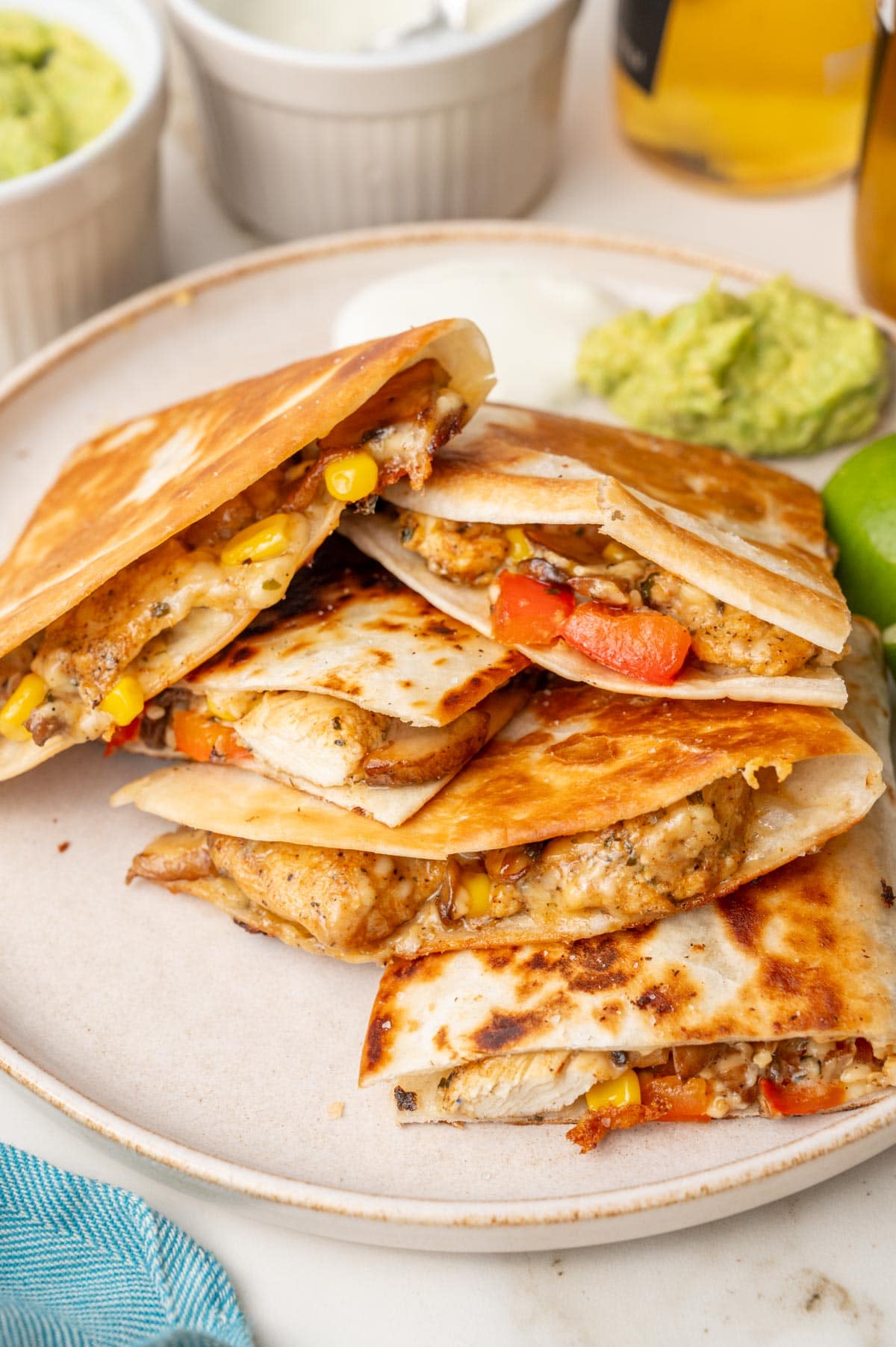 Chicken quesadillas on a beige plate- Guacamole, limes, beer in the background.