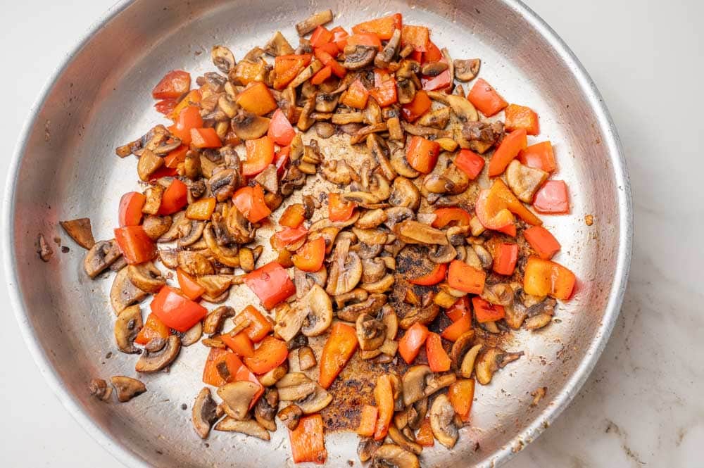 Sauteed bell pepper and mushrooms in a frying pan.
