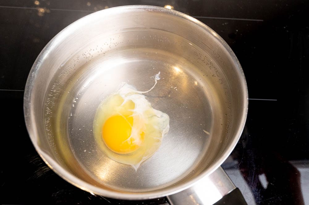 A raw egg is cooking in a small pot with simmering water.