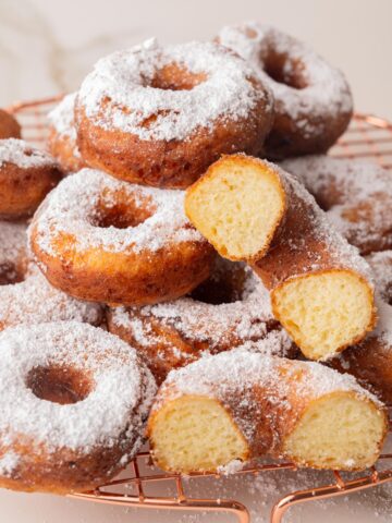 Polish cheese donuts (oponki) sprinkled with powdered sugar on a cooling rack.