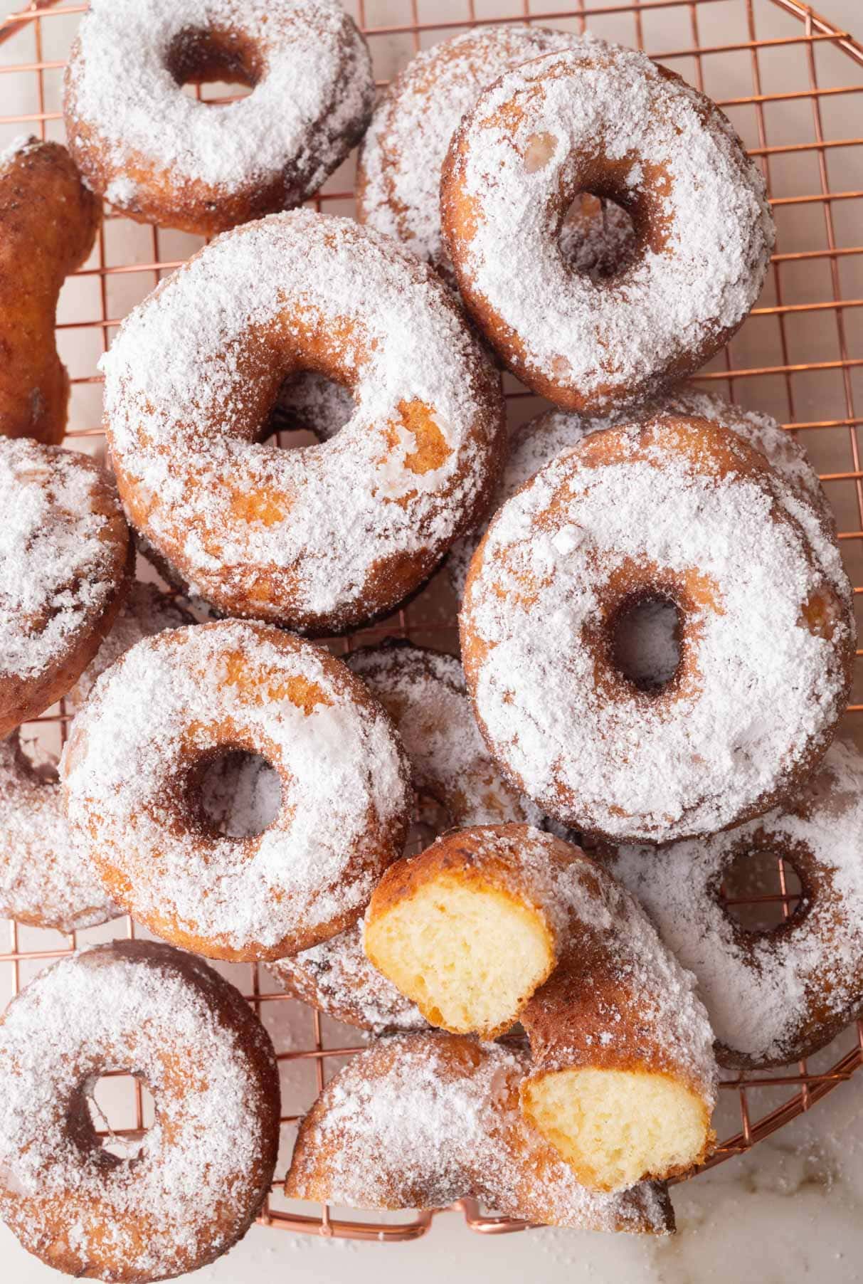An overhead photo of oponki donuts sprinkled with powdered sugar on a cooling rack.