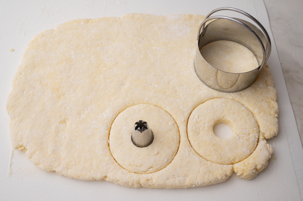 Rolled out dough on a rolling mat with donut shapes cut out.